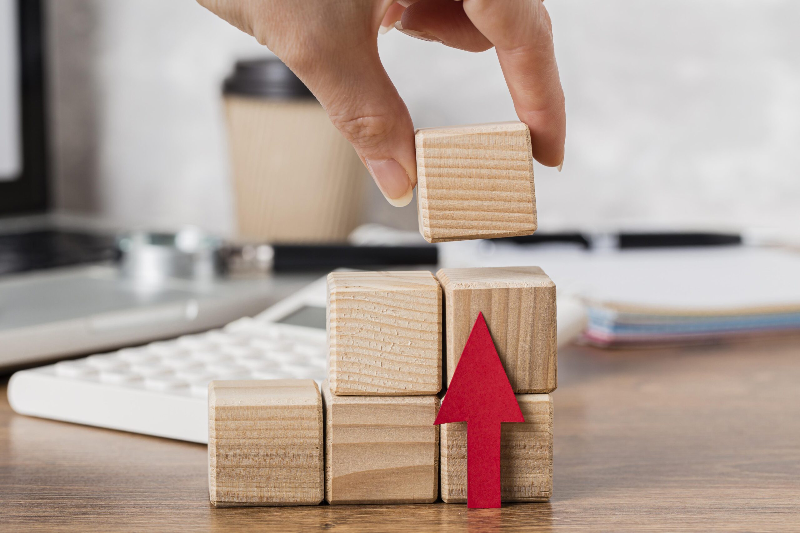 Some wooden building blocks in a staircase formation with a red arrow pointing up representing growth.